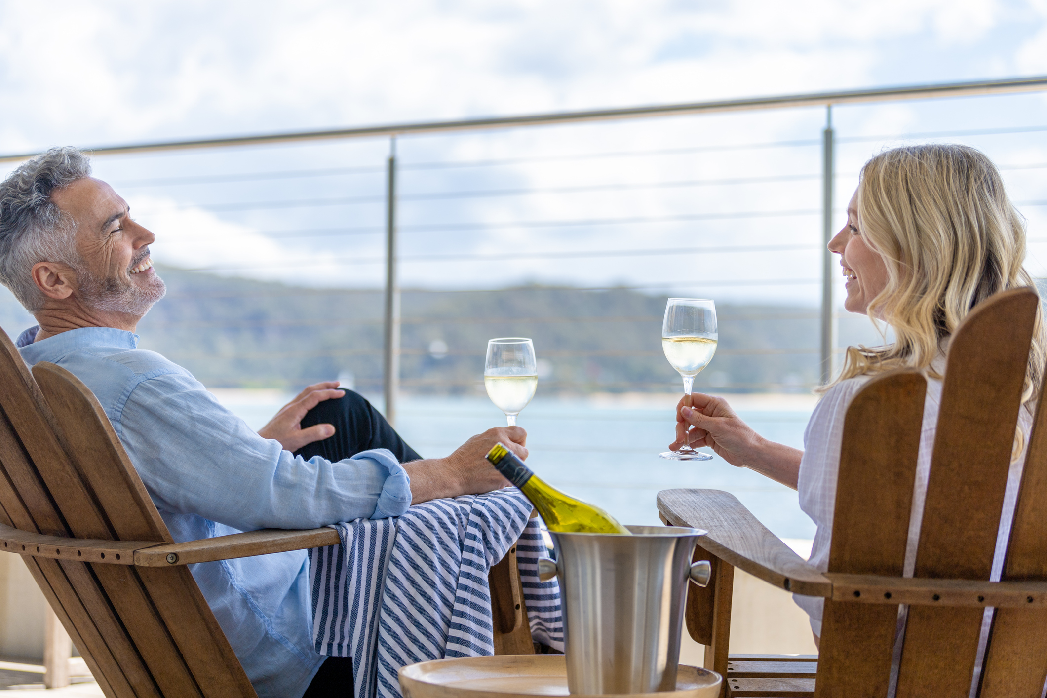 Couple d'âge mûr buvant du vin sur la terrasse. Ils sont heureux et souriants assis sur des transats. La mer est en arrière-plan.