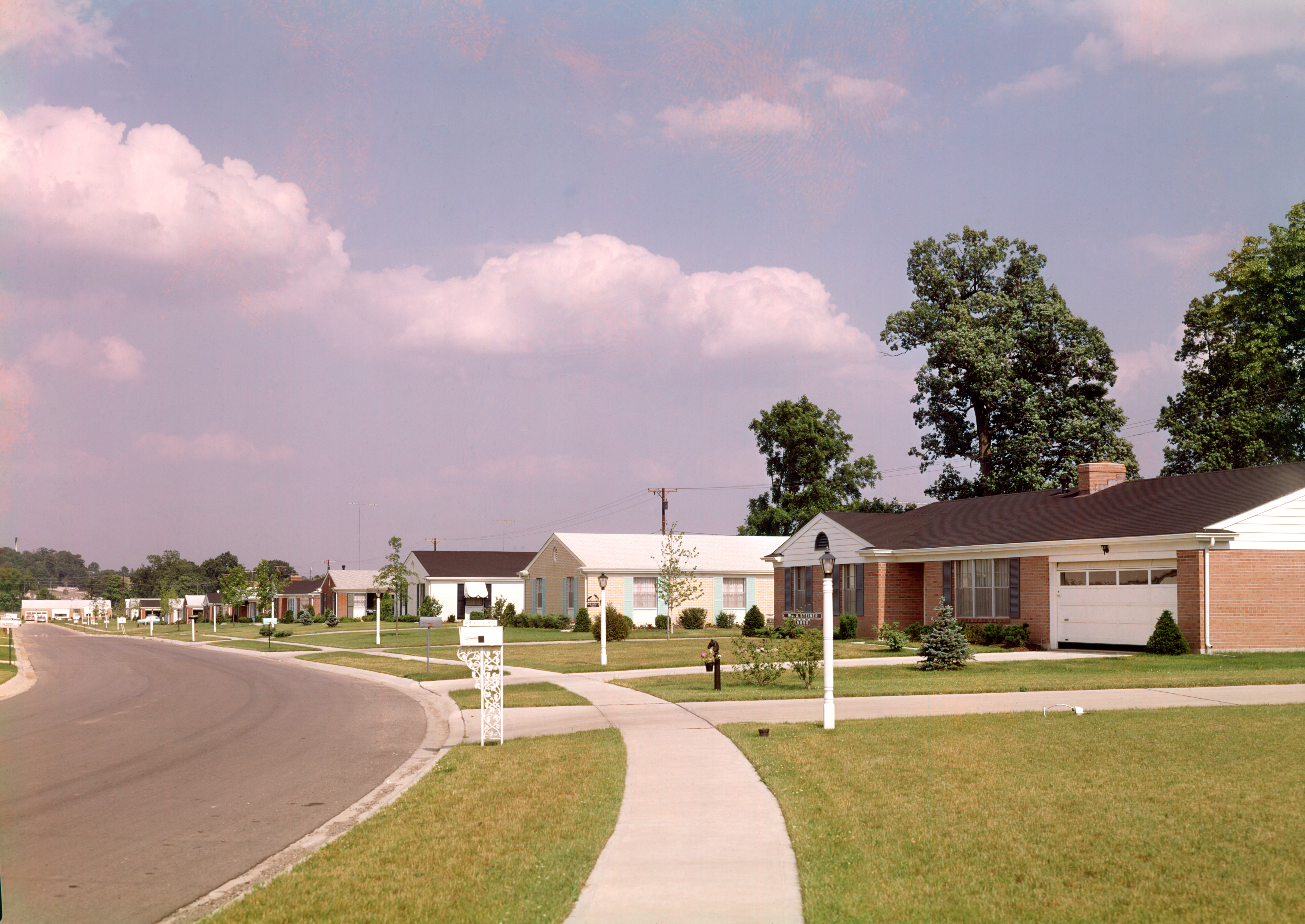 Un quartier de banlieue ca. Années 1960 ou 1970 avec des pelouses bien rangées et pas de voitures.