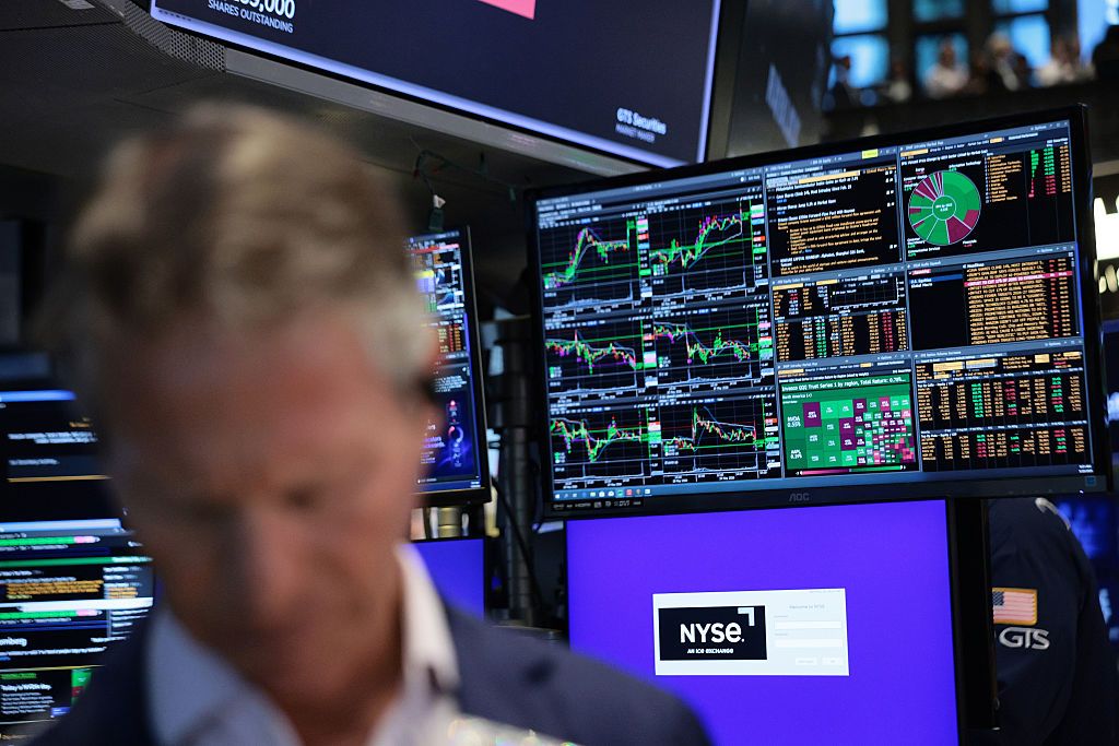 Close-up of a trader on the floor of the New York Stock Exchange (NYSE) with stock charts on a screen in the background
