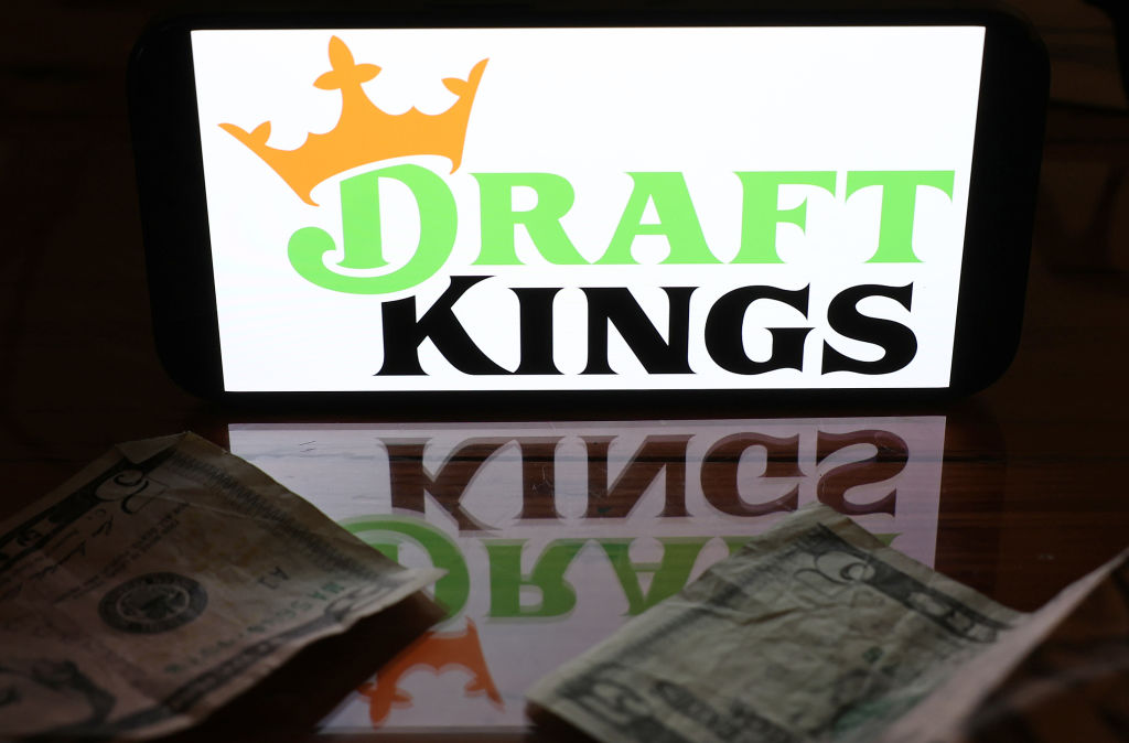 Logo DraftKings sur un smartphone reflété sur le dessus de table avec des billets de cinq dollars