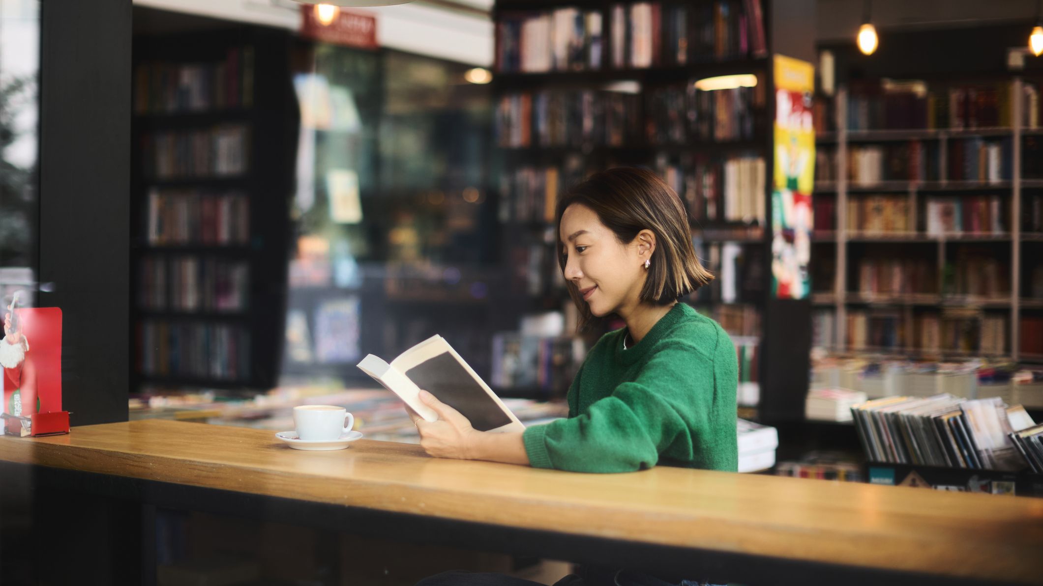 Une femme est assise dans un café près de la fenêtre et lit un livre avec une tasse de café