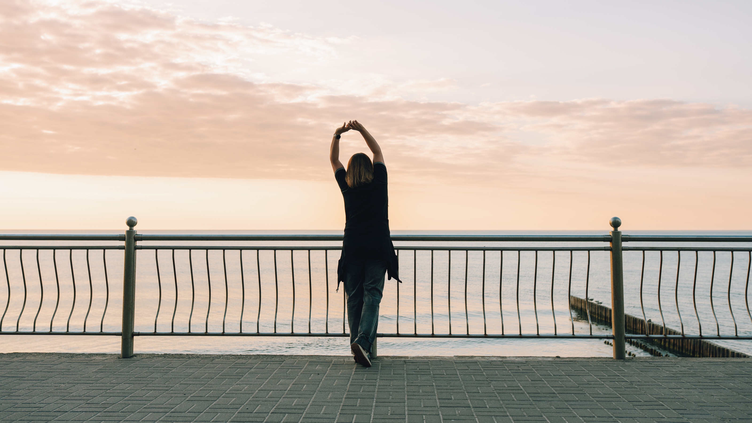 Une femme s’étend sur une promenade au bord de la mer au lever du soleil.
