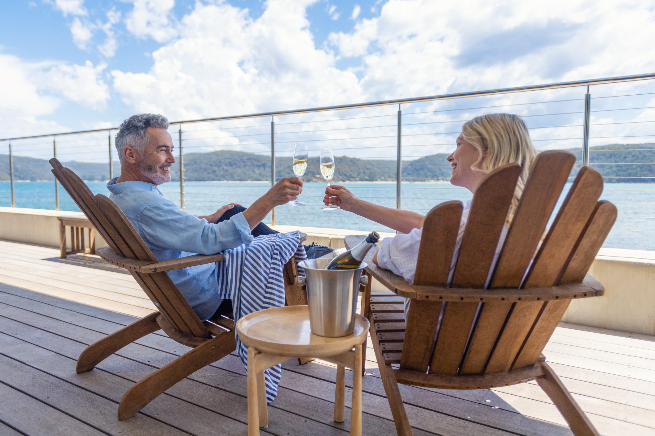 Couple d'âge mûr buvant du champagne sur le pont. Ils sont heureux et souriants assis sur des transats. La mer est en arrière-plan
