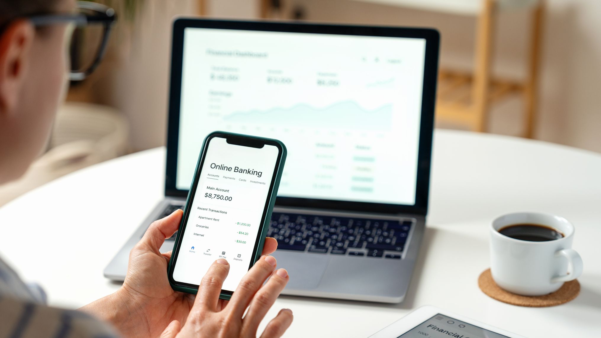 Utilisateur accédant aux services bancaires numériques via un smartphone et un ordinateur portable à la maison