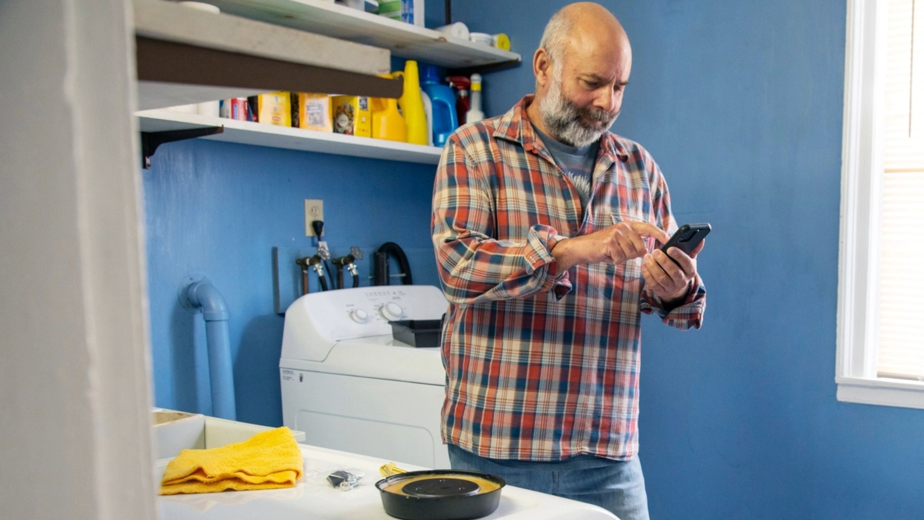 Un homme mûr utilise son smartphone tout en faisant du bricolage dans la buanderie