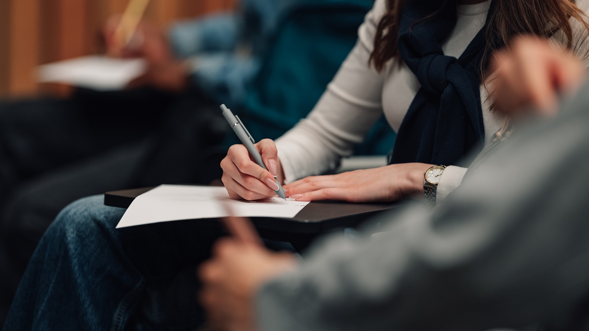 Une personne prend des notes lors d’une conférence, seuls ses mains et son papier étant visibles.