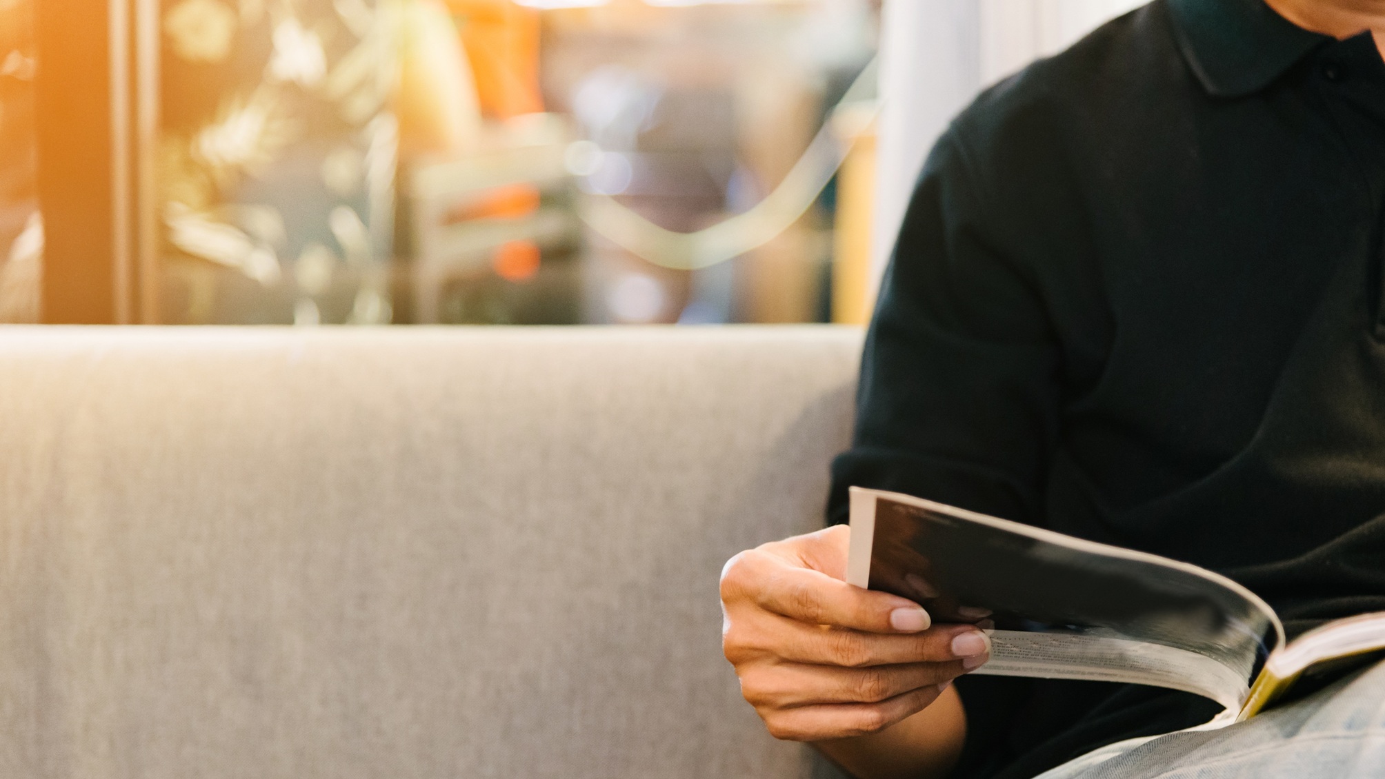 Un homme lisant un magazine sur un canapé.