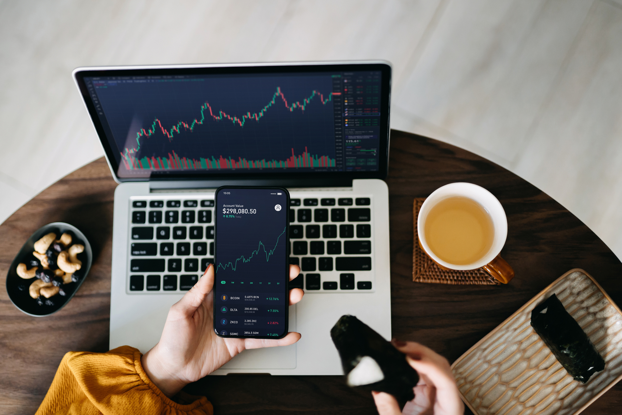 Une femme tenant un smartphone, analysant les données de trading d'investissement tout en déjeunant, travaillant à la maison.