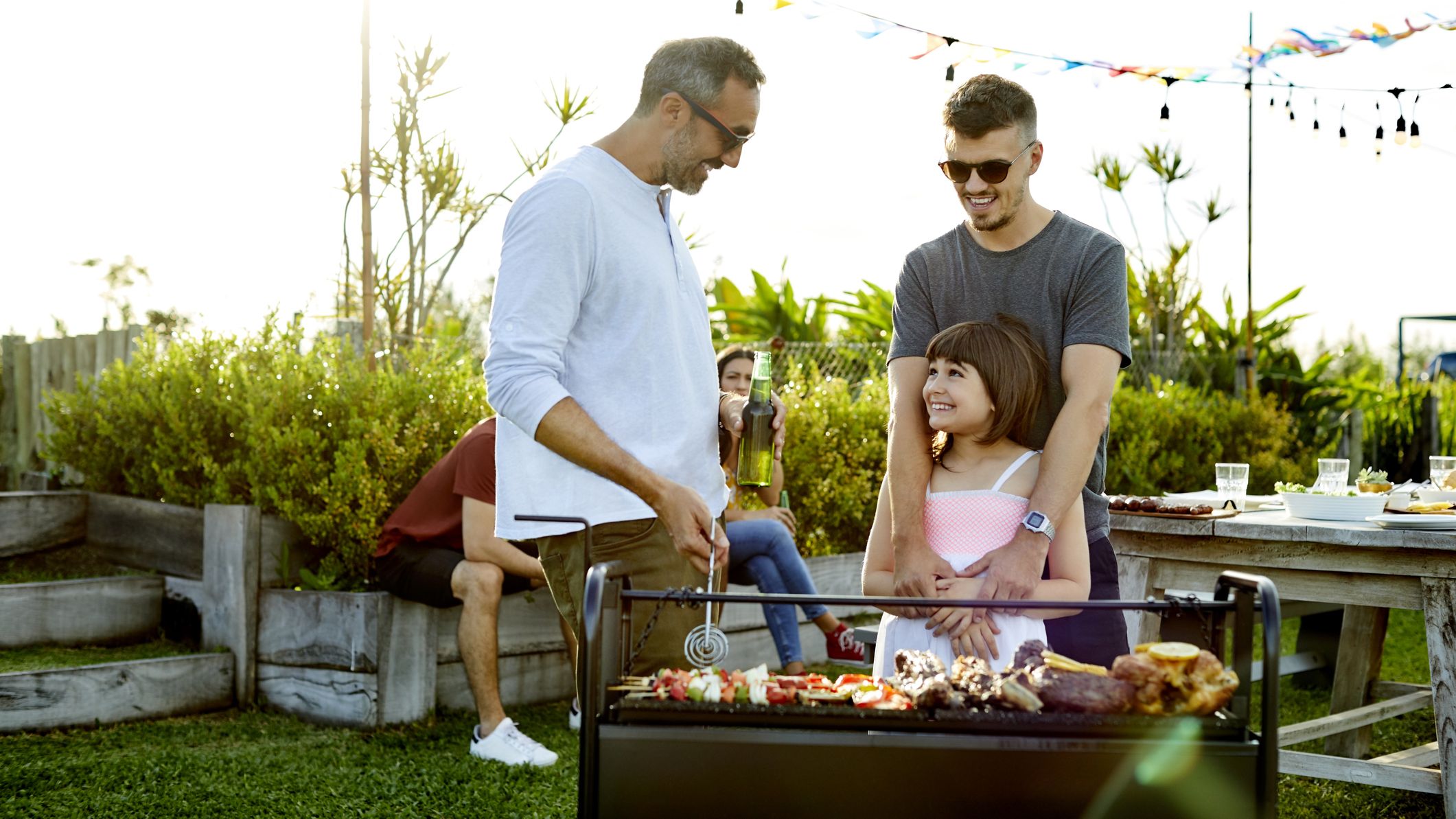 Homme parlant avec une fille souriante tout en préparant de la nourriture sur un barbecue.
