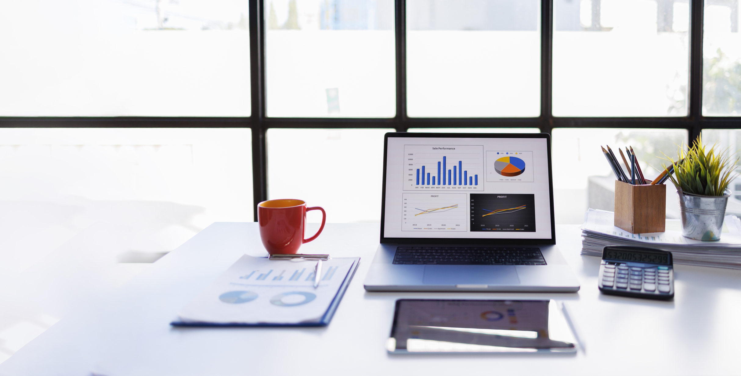 un bureau avec une tasse de café, des projections financières et un ordinateur portable ouvert avec des graphiques à barres et des diagrammes circulaires