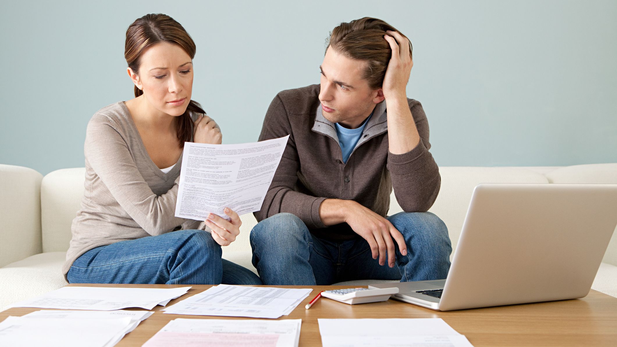 Un couple discute de son budget domestique avec des documents et un ordinateur portable sur la table.