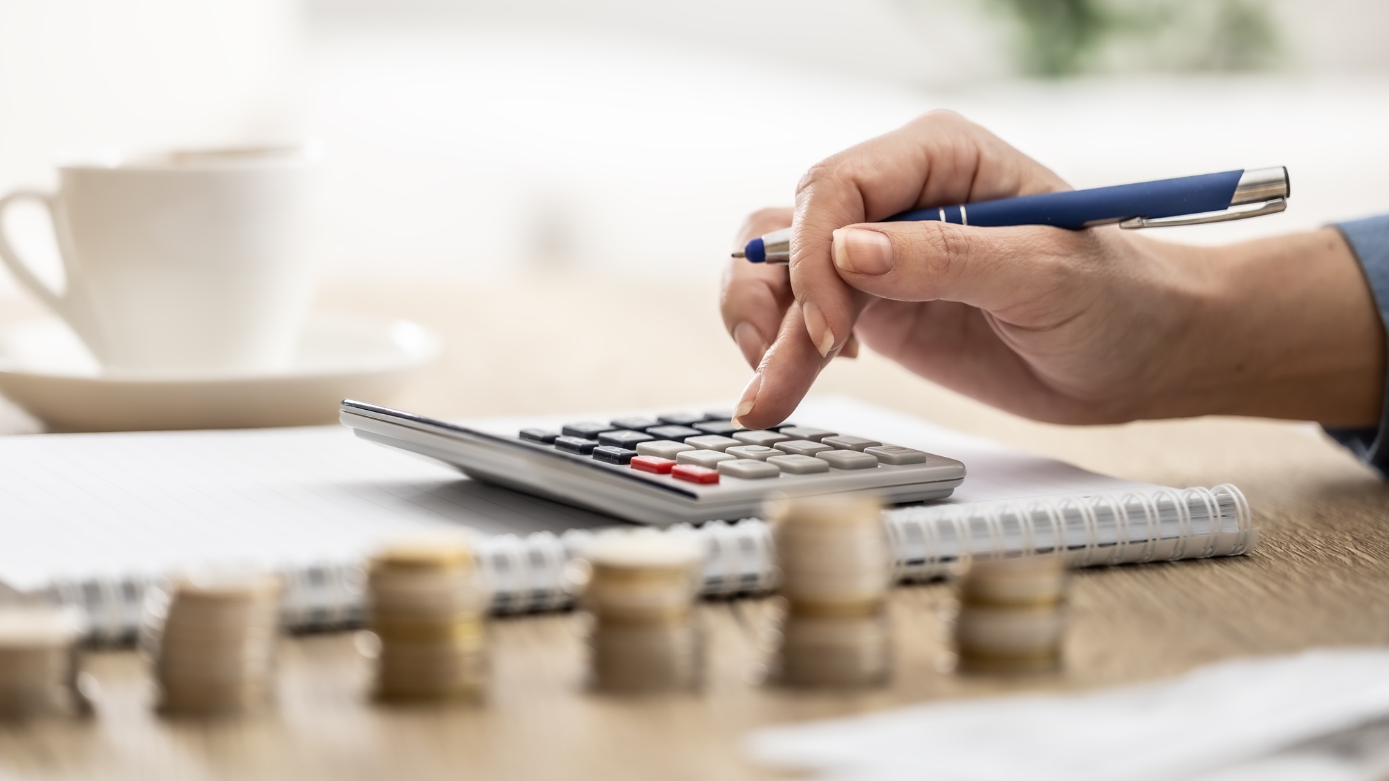 Une femme utilise une calculatrice à côté de piles de pièces de différentes hauteurs.