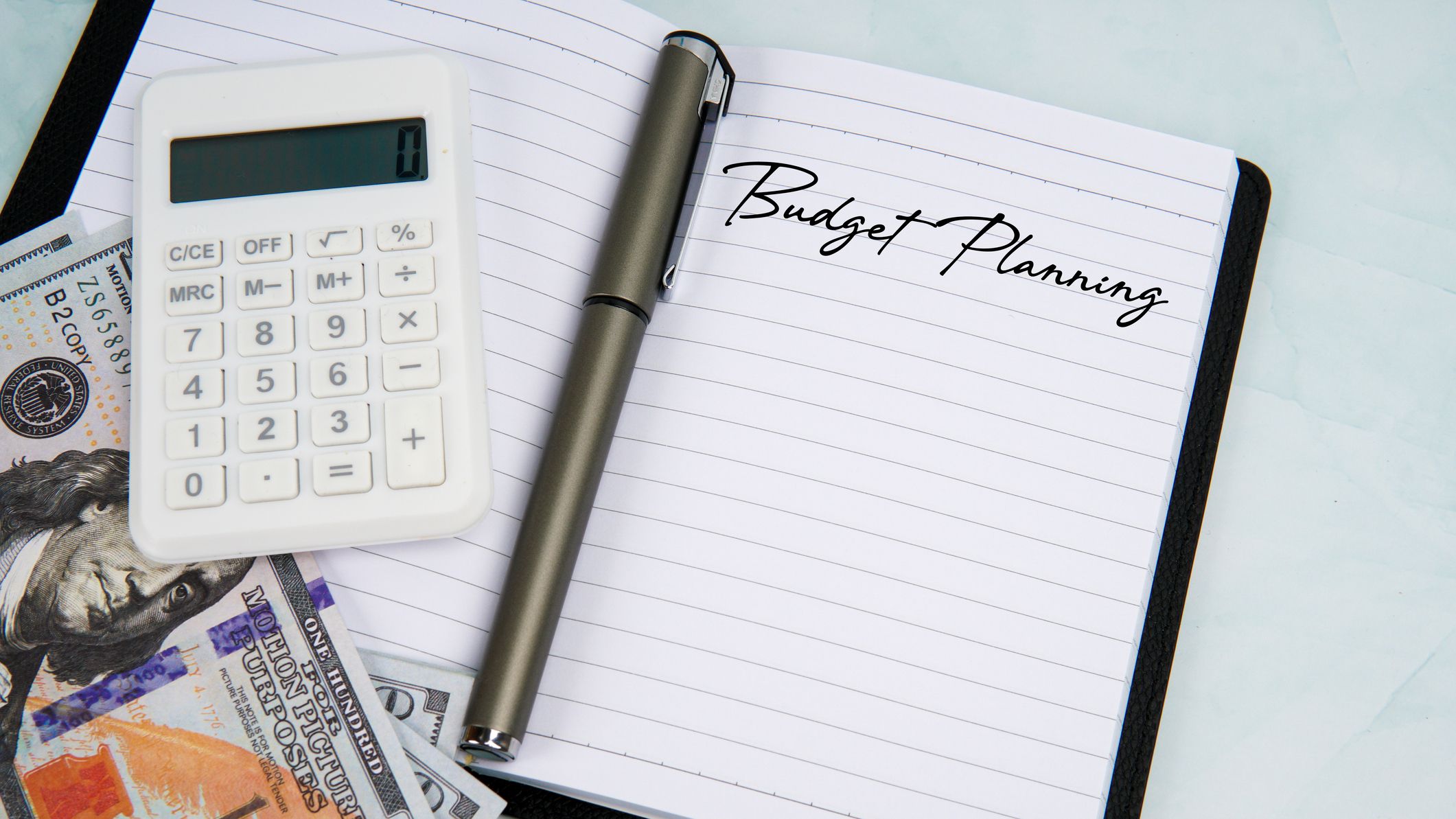 Carnet avec texte de planification budgétaire à côté d'une calculatrice, d'un stylo et de billets en dollars américains