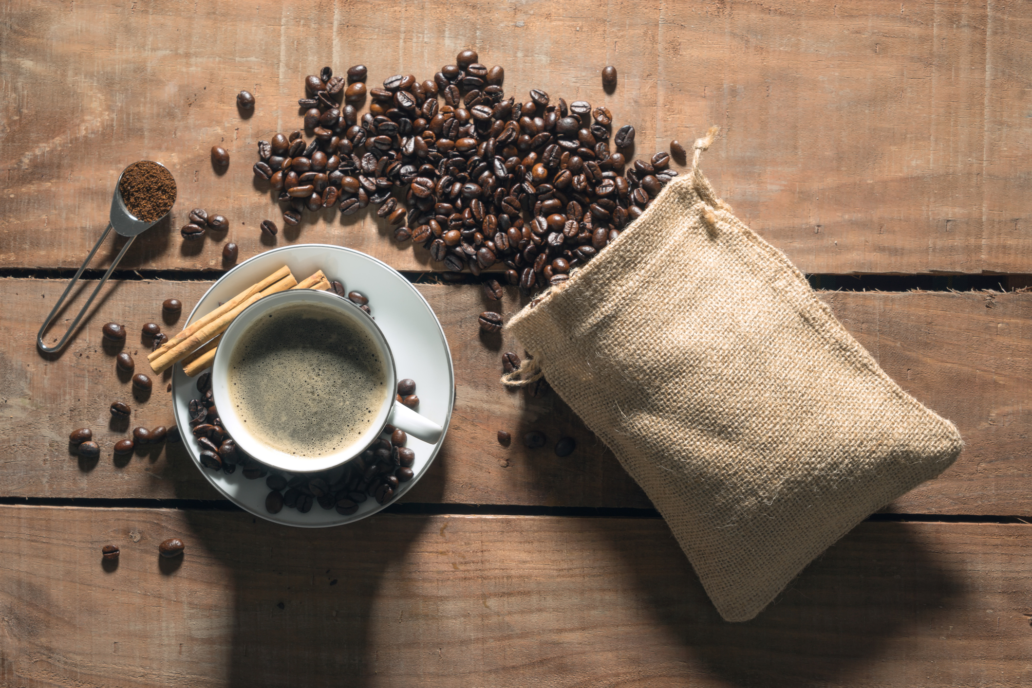 un sac en toile de jute rempli de grains de café à côté d'une tasse de café sur une soucoupe