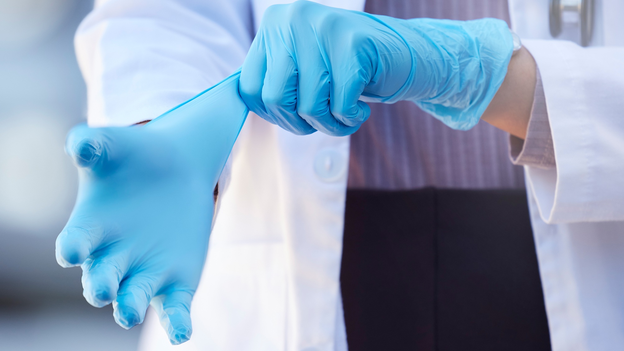 Un médecin enfile des gants stériles, seules ses mains sont visibles.