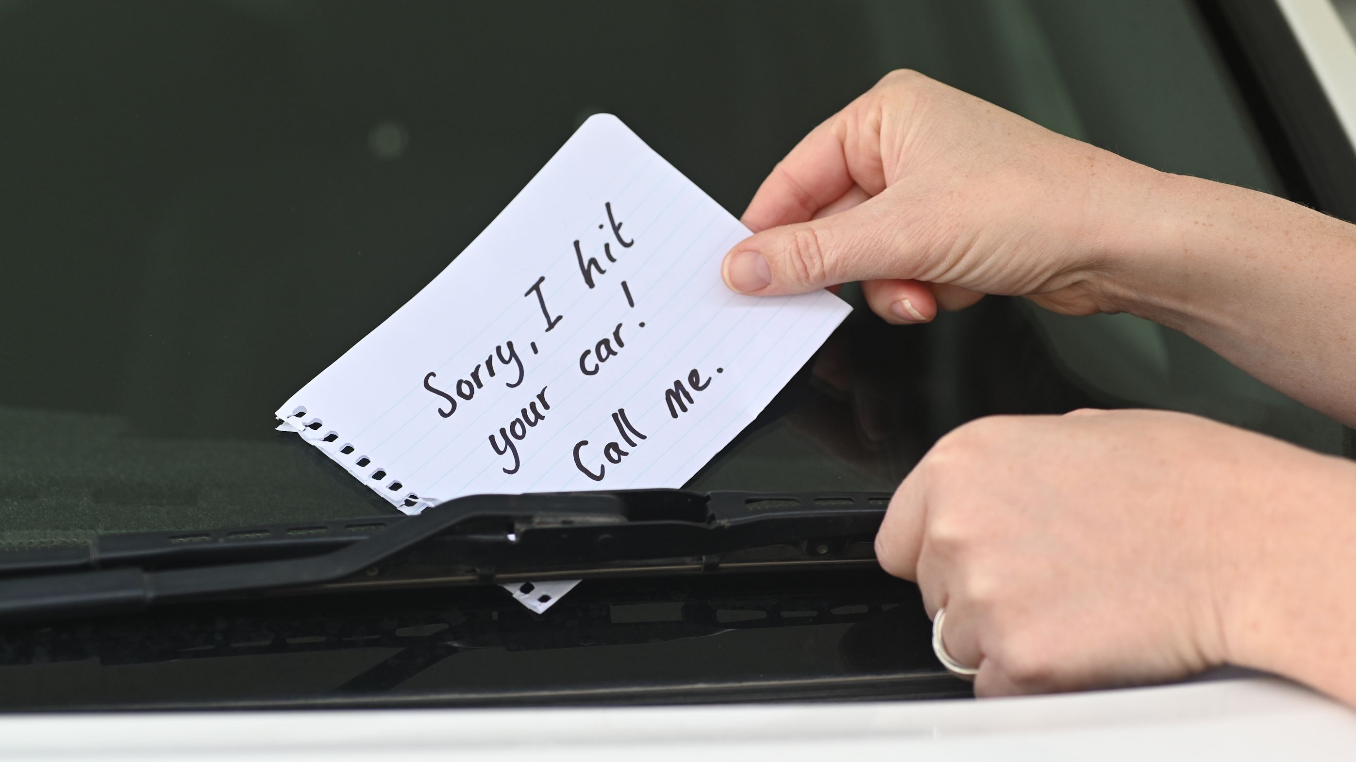 Une personne laissant une note sur une voiture après l'avoir heurtée.