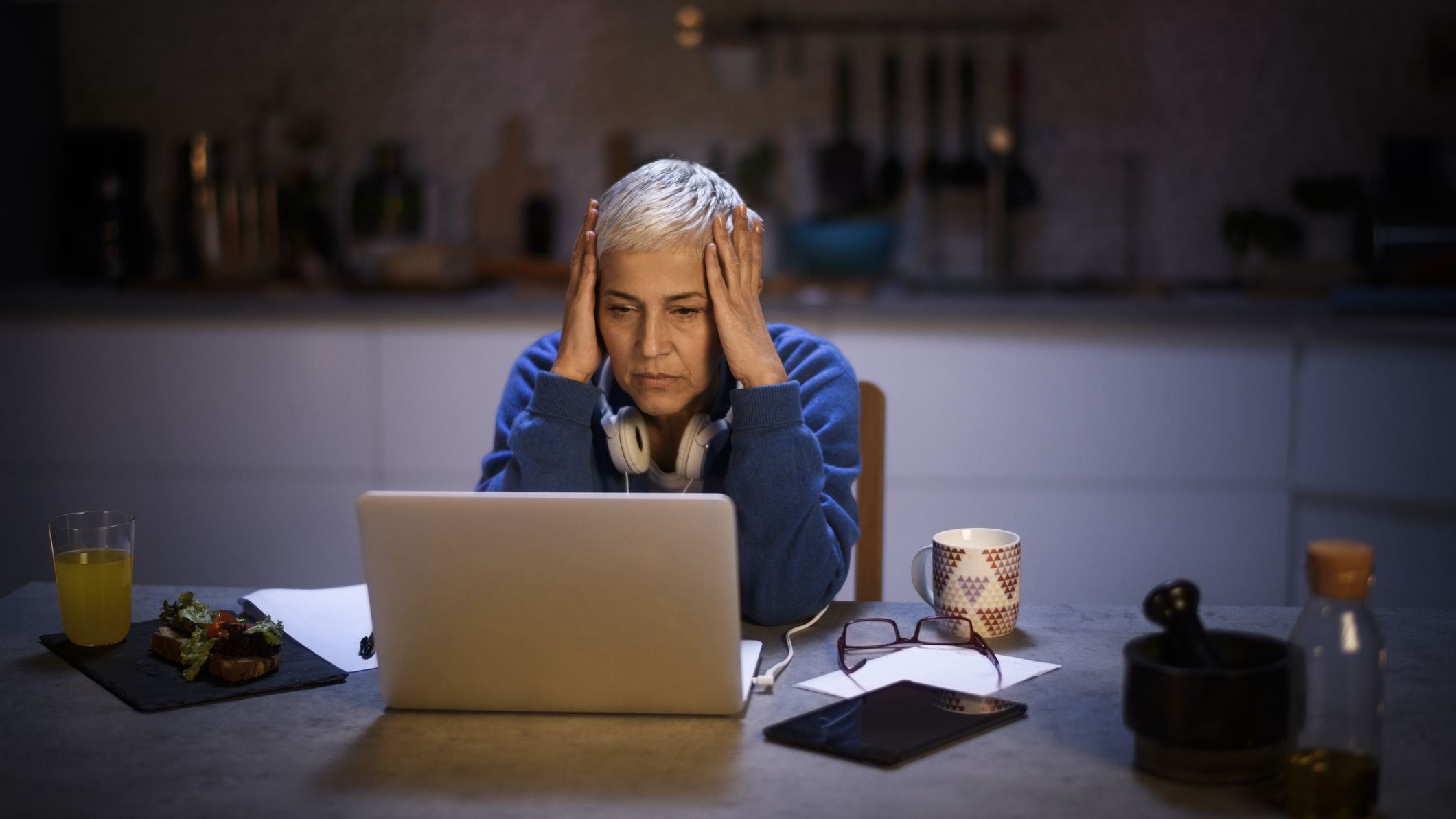 Une femme âgée dans une cuisine sombre, stressée par ses finances.