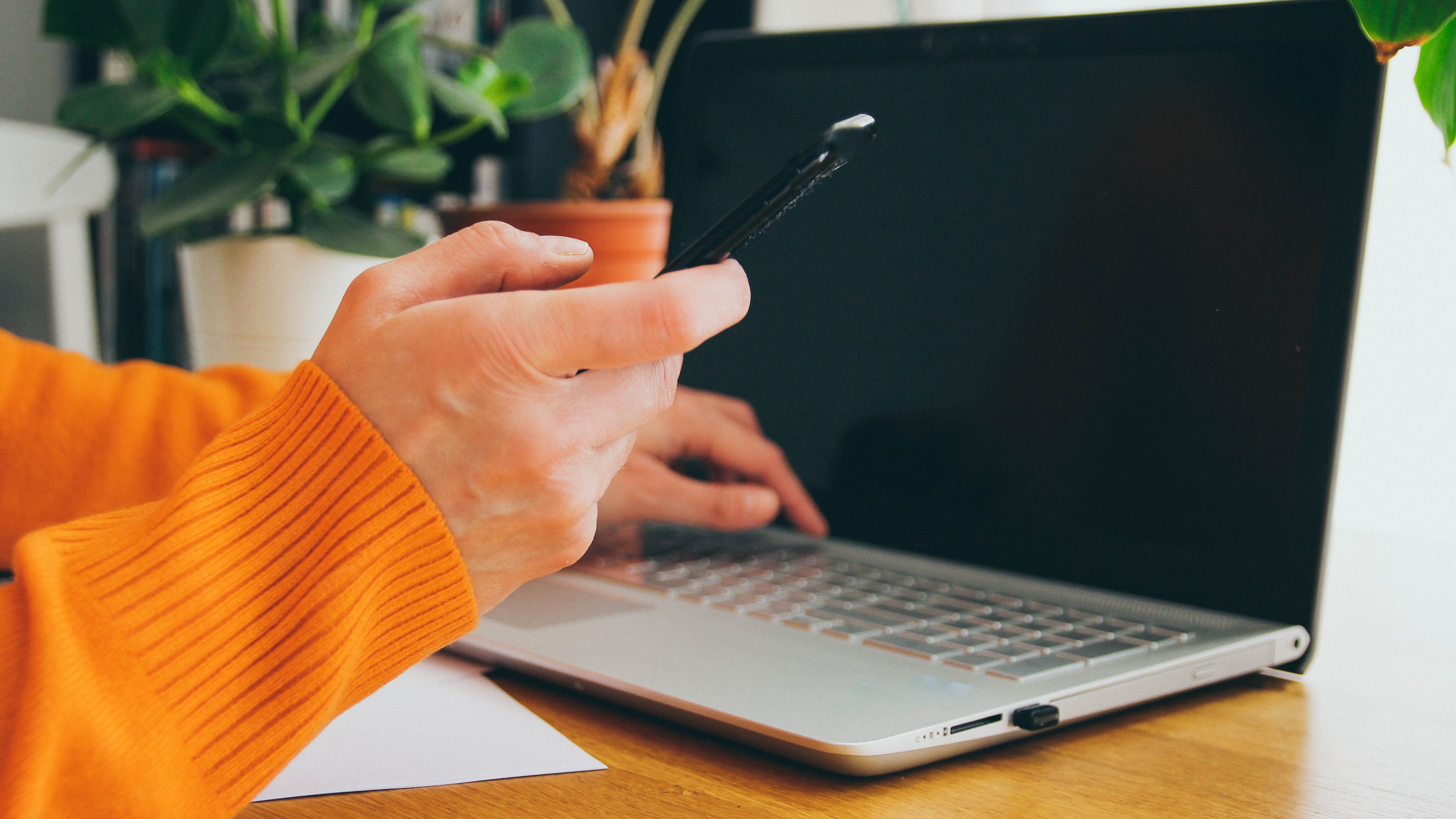 Une personne tient son smartphone tout en travaillant sur un ordinateur portable.