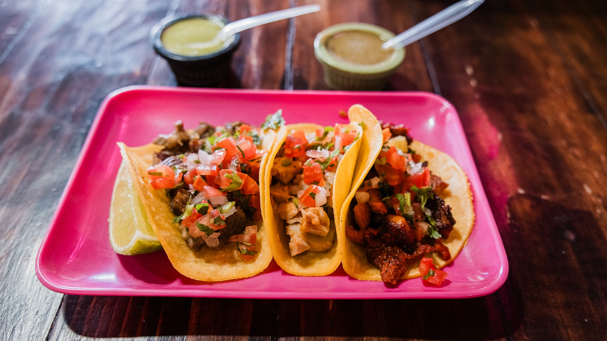 Trois tacos de rue et une assiette carrée rose dans un restaurant.