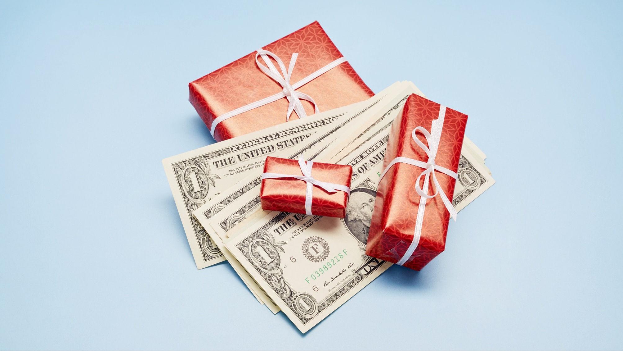 De petites boîtes enveloppées de rouge avec des nœuds blancs et mélangées à des billets d'un dollar.