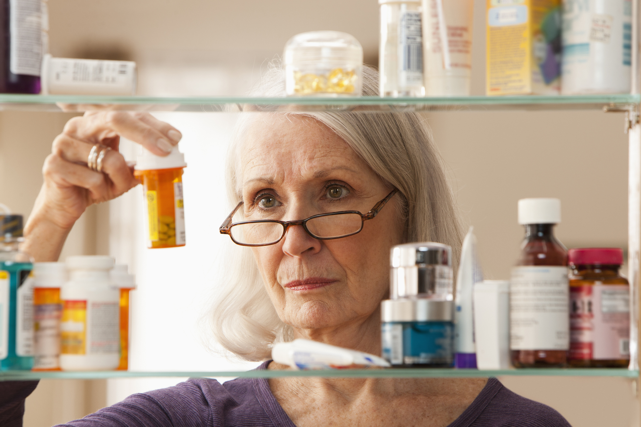 Une femme mûre inspecte les flacons de médicaments dans son armoire à pharmacie.