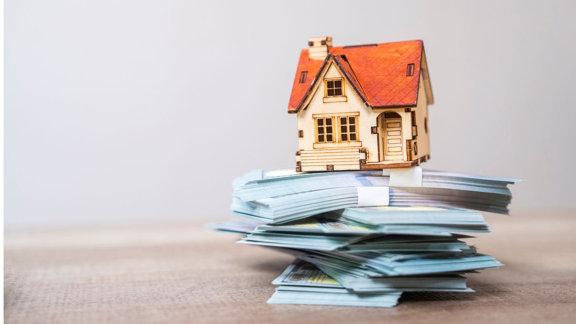 Une maison modèle posée au sommet d’une pile d’argent liquide.