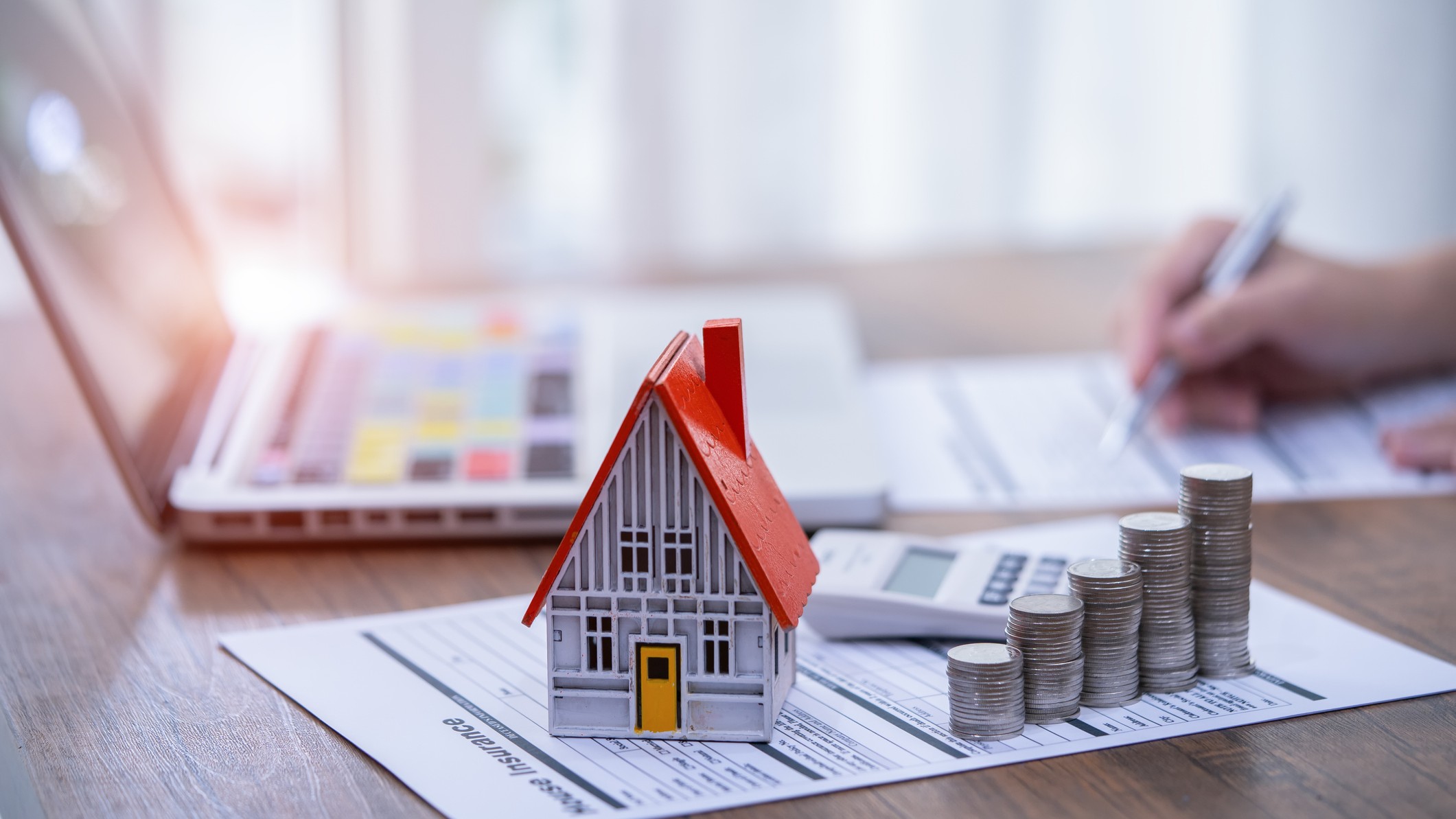 une maison modèle, une calculatrice et une pile de pièces posées sur une demande de prêt hypothécaire