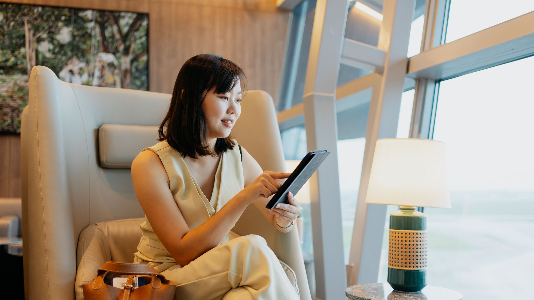 Une femme d'affaires se détend dans un salon d'aéroport avec un capuccino et une tablette.