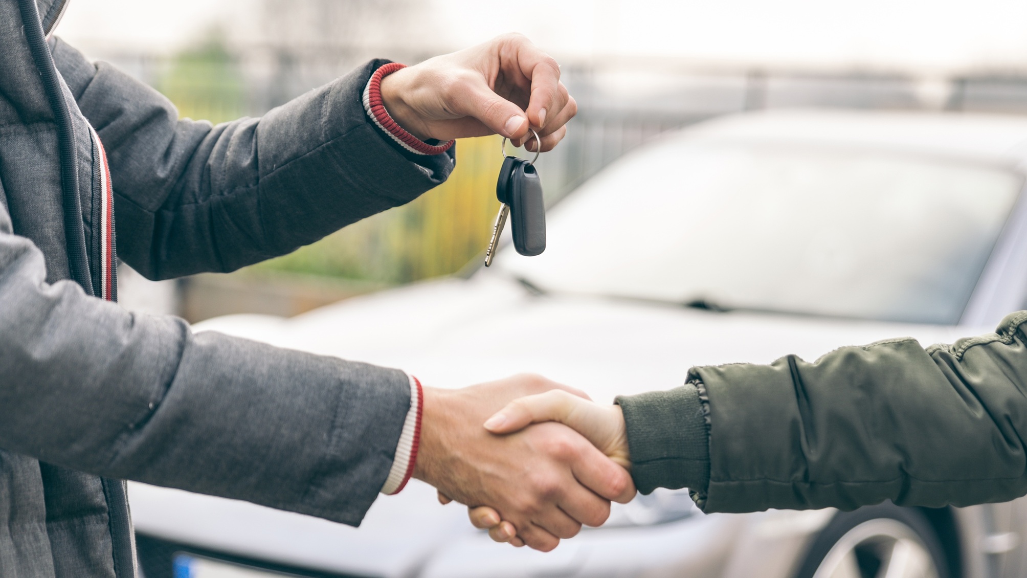 Un concessionnaire automobile remet les clés d'une voiture neuve et serre la main de l'acheteur.