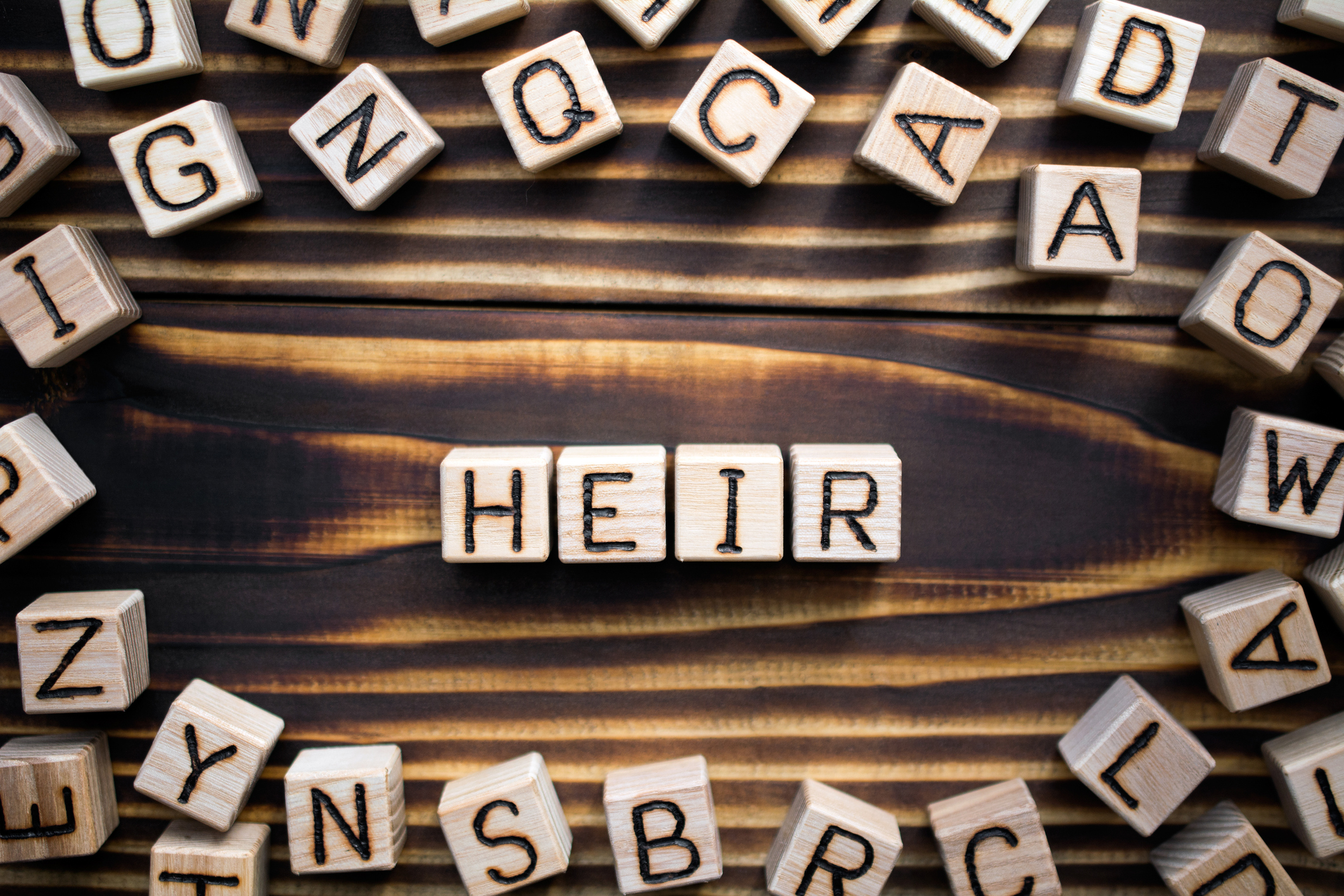 mot héritier composé de cubes en bois avec des lettres, avec des lettres aléatoires dispersées, vue de dessus sur fond en bois