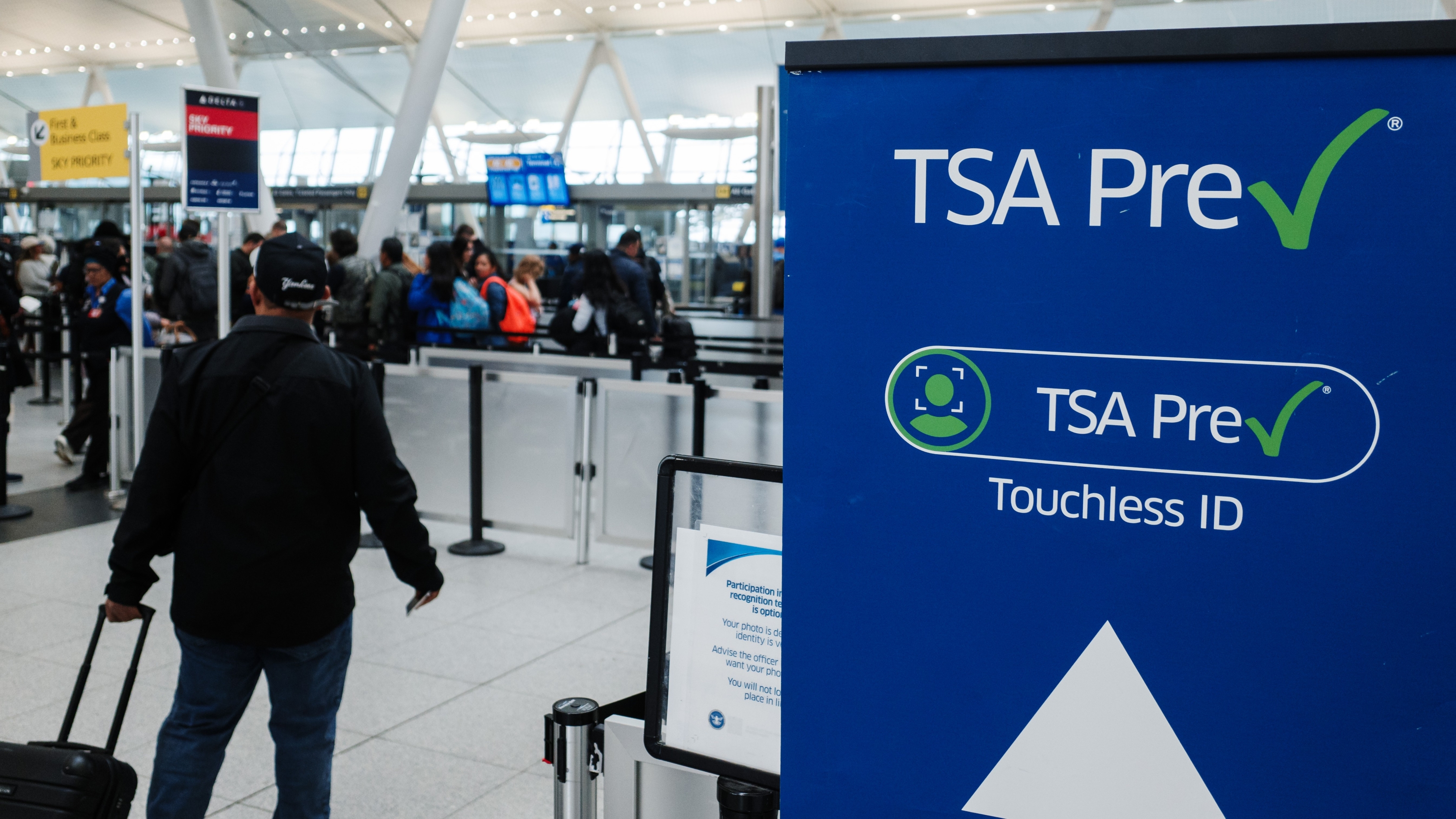Un voyageur avec une valise à roulettes se dirige vers la voie TSA PreCheck Touchless ID.