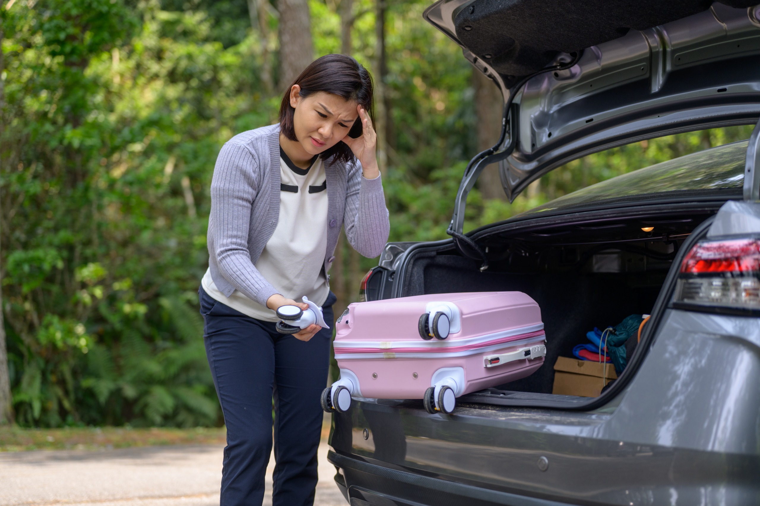 Une femme stressée examine une roue cassée de sa valise.