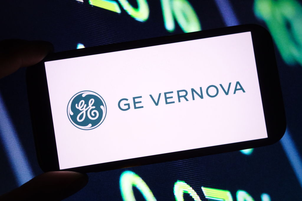 Logo GE Vernova sur smartphone avec tableau téléscripteur en arrière-plan