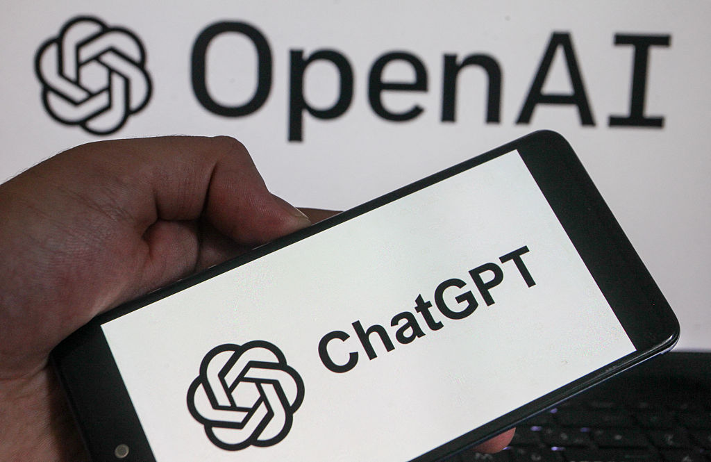 Un smartphone affichant les logos de la société technologique américaine OpenAI et de son assistant d'intelligence artificielle ChatGPT tenu dans une main.