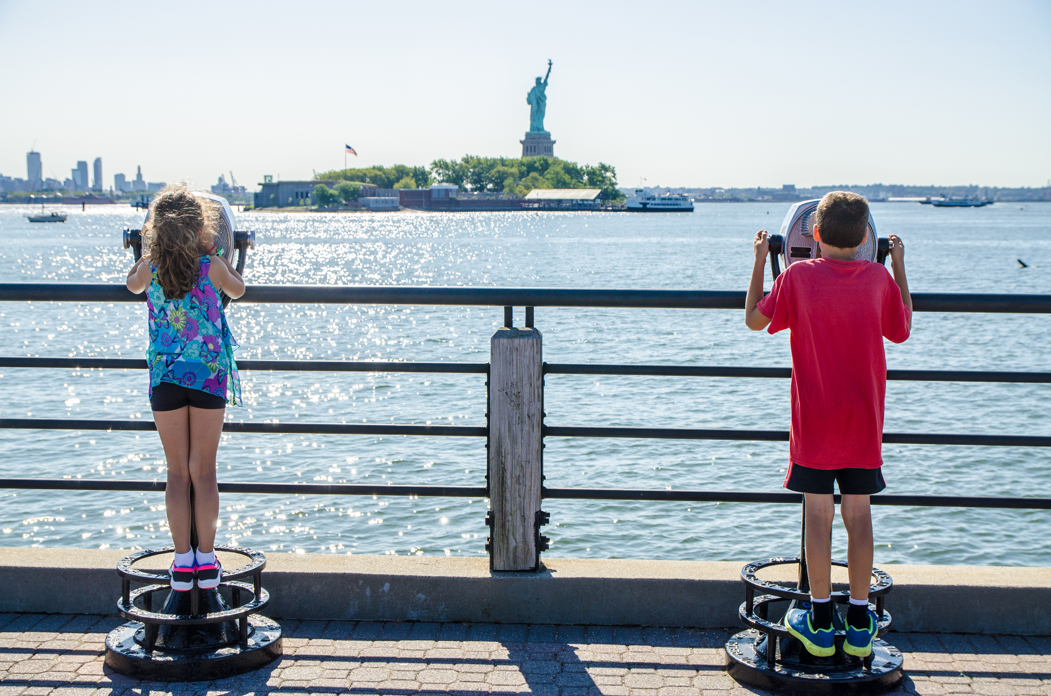 Des enfants regardent la Statue de la Liberté à l'aide de jumelles payantes depuis le Liberty State Park à Jersey City pendant la journée d'été