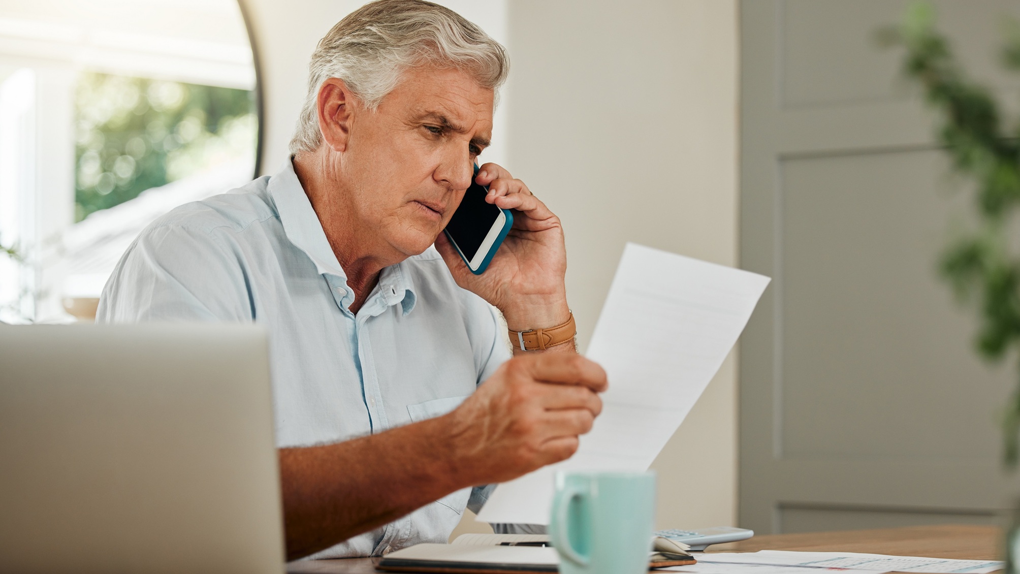 Un homme plus âgé consulte des documents tout en parlant au téléphone.
