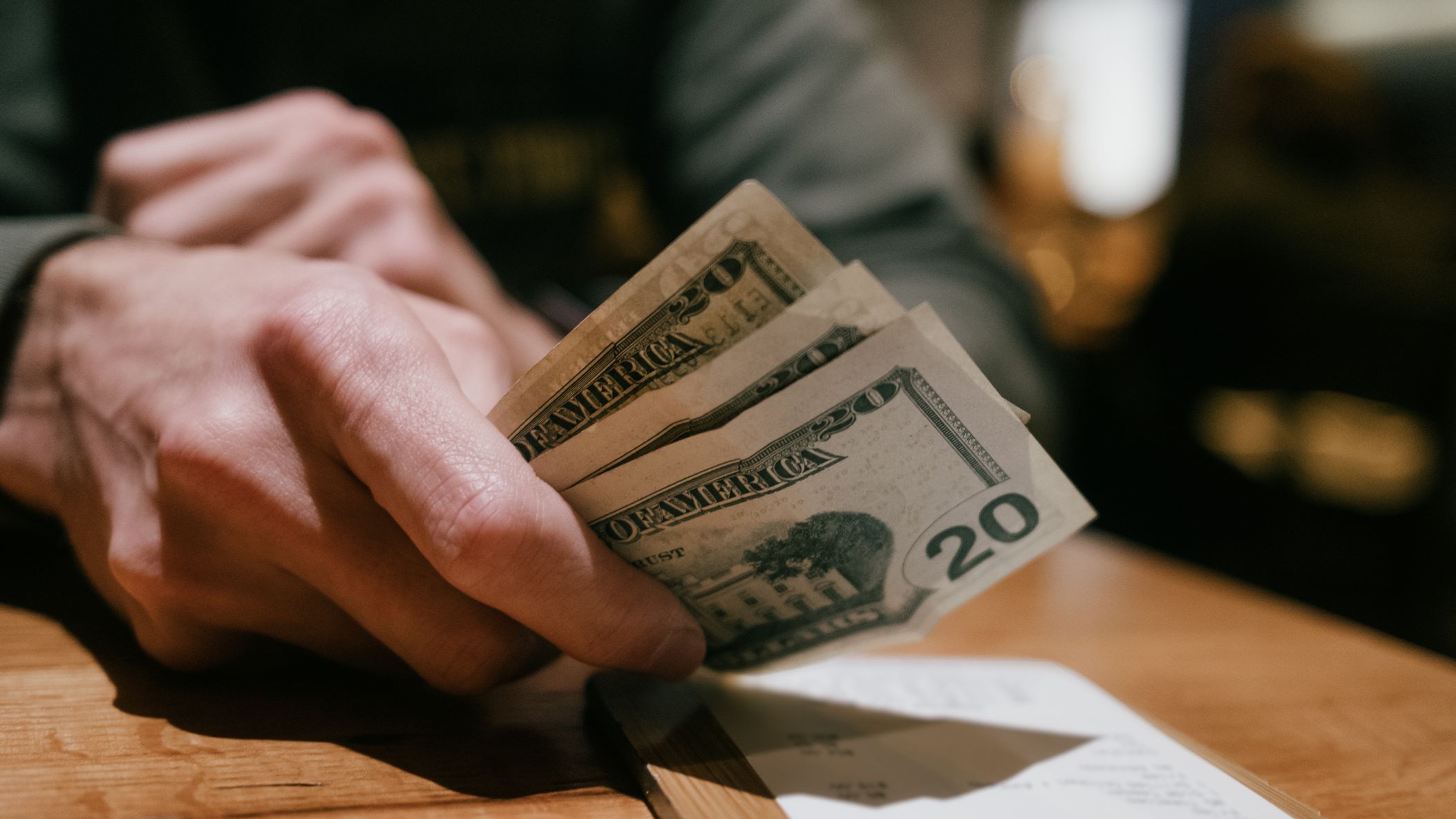 un homme dépose trois billets de 20 $ pour payer une note de restaurant