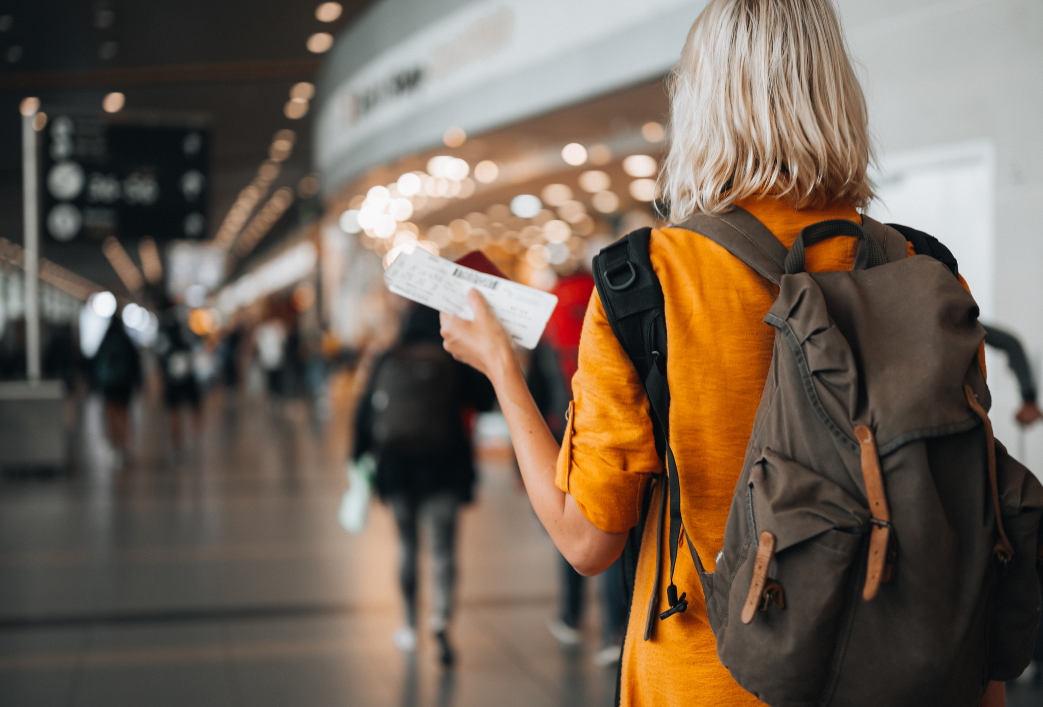 Vue arrière d'une femme à l'aéroport détenant un passeport avec une carte d'embarquement alors qu'elle se dirige vers sa porte d'embarquement