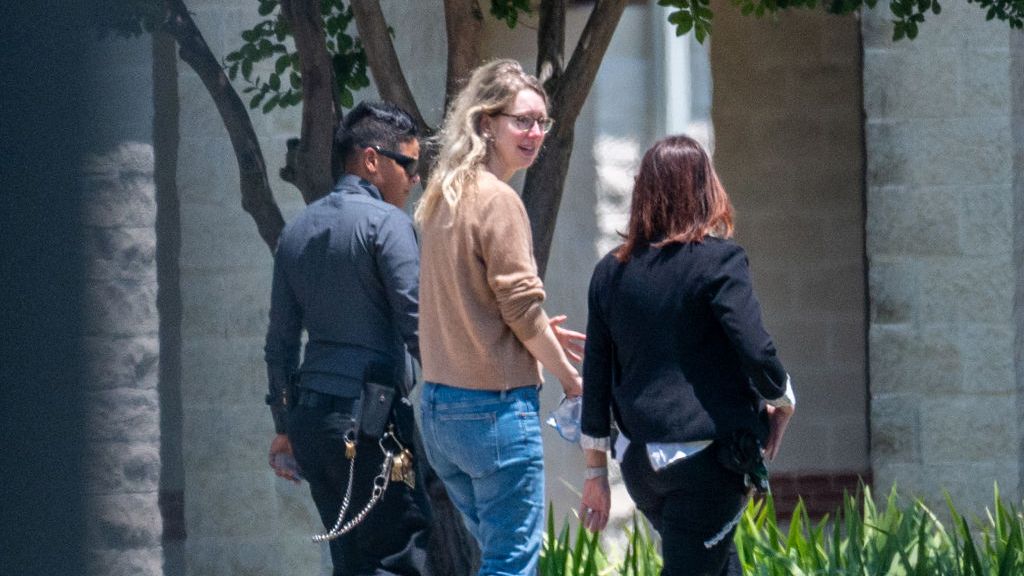 Elizabeth Holmes, vêtue d'un pull marron et d'un jean, entre dans un camp de prisonniers fédéral.