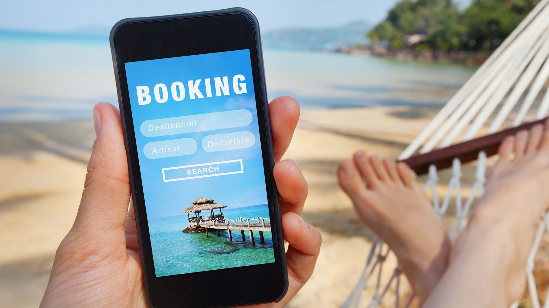 Une personne regarde un téléphone avec un voyage "réservation" écran en étant allongé sur un hamac sur une plage.